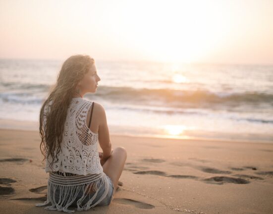 woman in a lace blouse sitting on a sandy beach