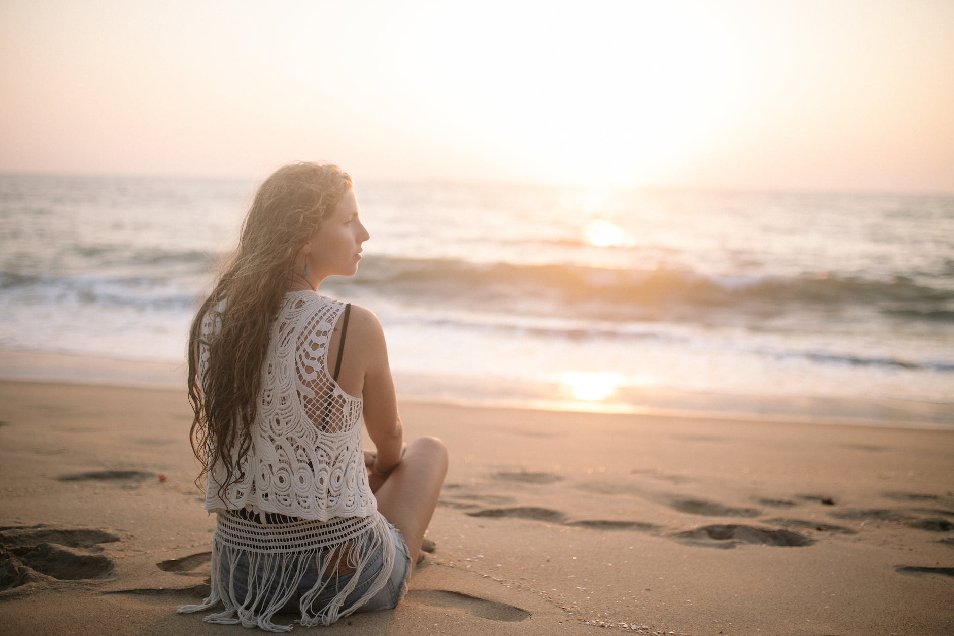 woman in a lace blouse sitting on a sandy beach