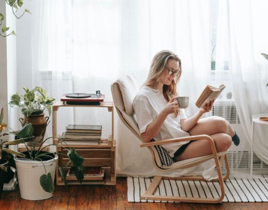 smiling woman with hot drink reading book at home