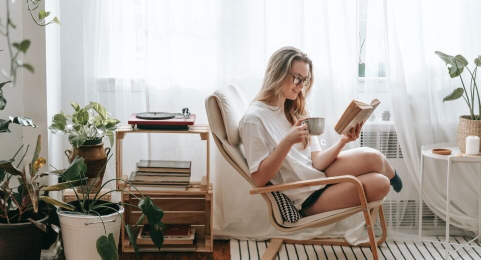 smiling woman with hot drink reading book at home